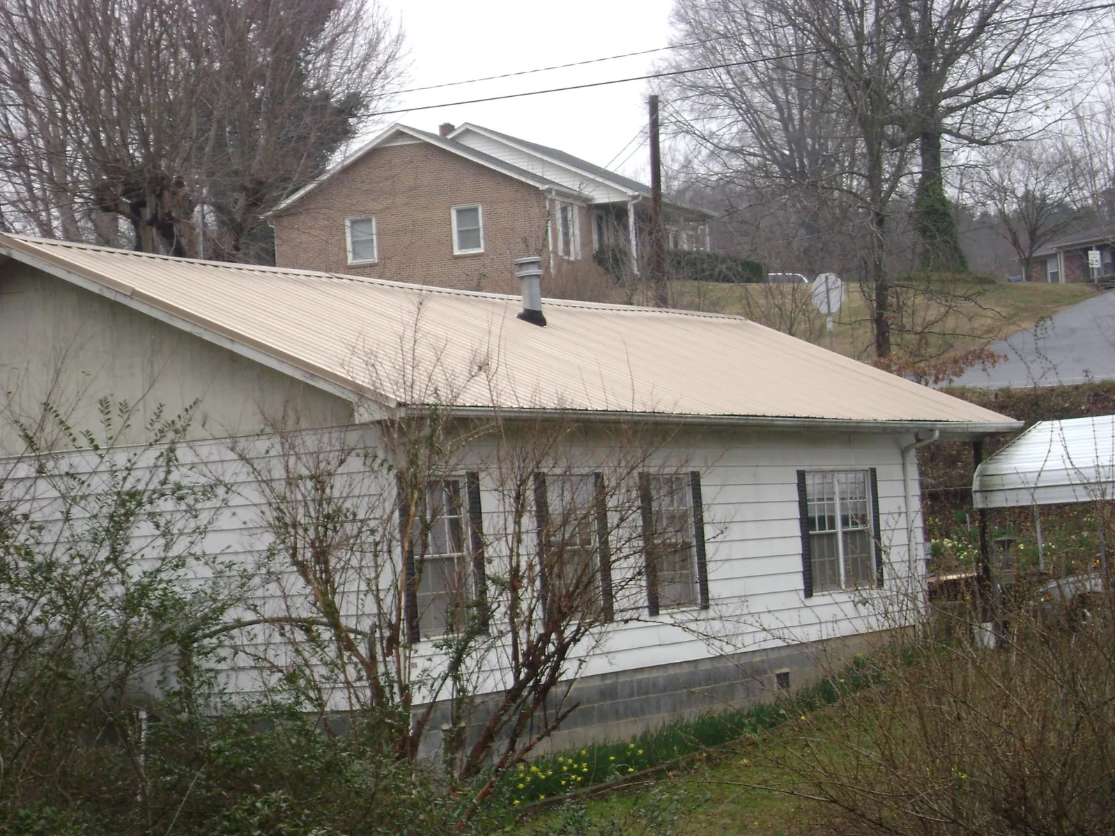 Tan metal roof on a white sided house set into a hillside — Commercial Roofing by Roofing Brothers in Naval Anacost Annex