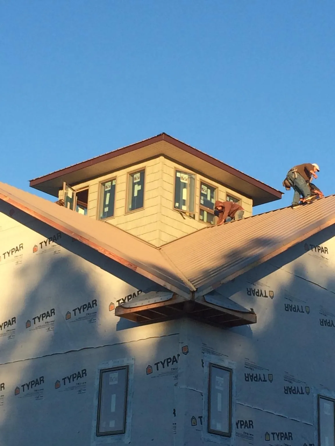 Roofers working around a rooftop cupola on a new metal roof at sunset in Naval Anacost Annex